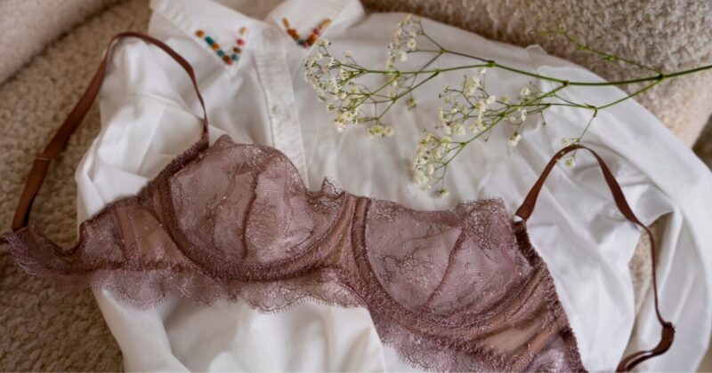 白いシャツとカスミソウの上に置かれた、繊細なモーヴピンクのレースブラジャー。上質なランジェリーによる優雅で心地よい時間を表現したイメージ。